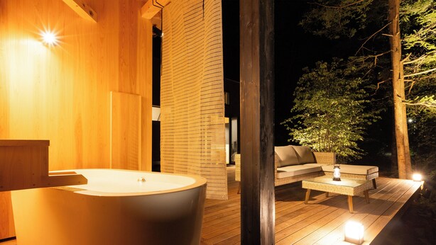 Ein modernes Badezimmer im Freien mit einer großen Badewanne, einer Holzterrasse und einer Sitzecke mit Tisch und Stühlen.