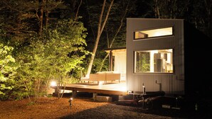 Eine moderne, zweistöckige Holzhütte mit einer Terrasse, umgeben von Bäumen.