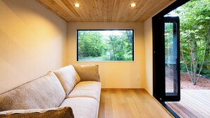 Ein modernes Interieur mit Holzboden, einer großen Fensterfront mit Blick auf einen Wald und einer Holzzielung.