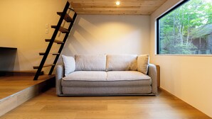 Ein modernes Wohnzimmer mit grauem Sofa, Holzboden, Holzzieldecke und einem großen Fenster mit Blick auf Bäume.