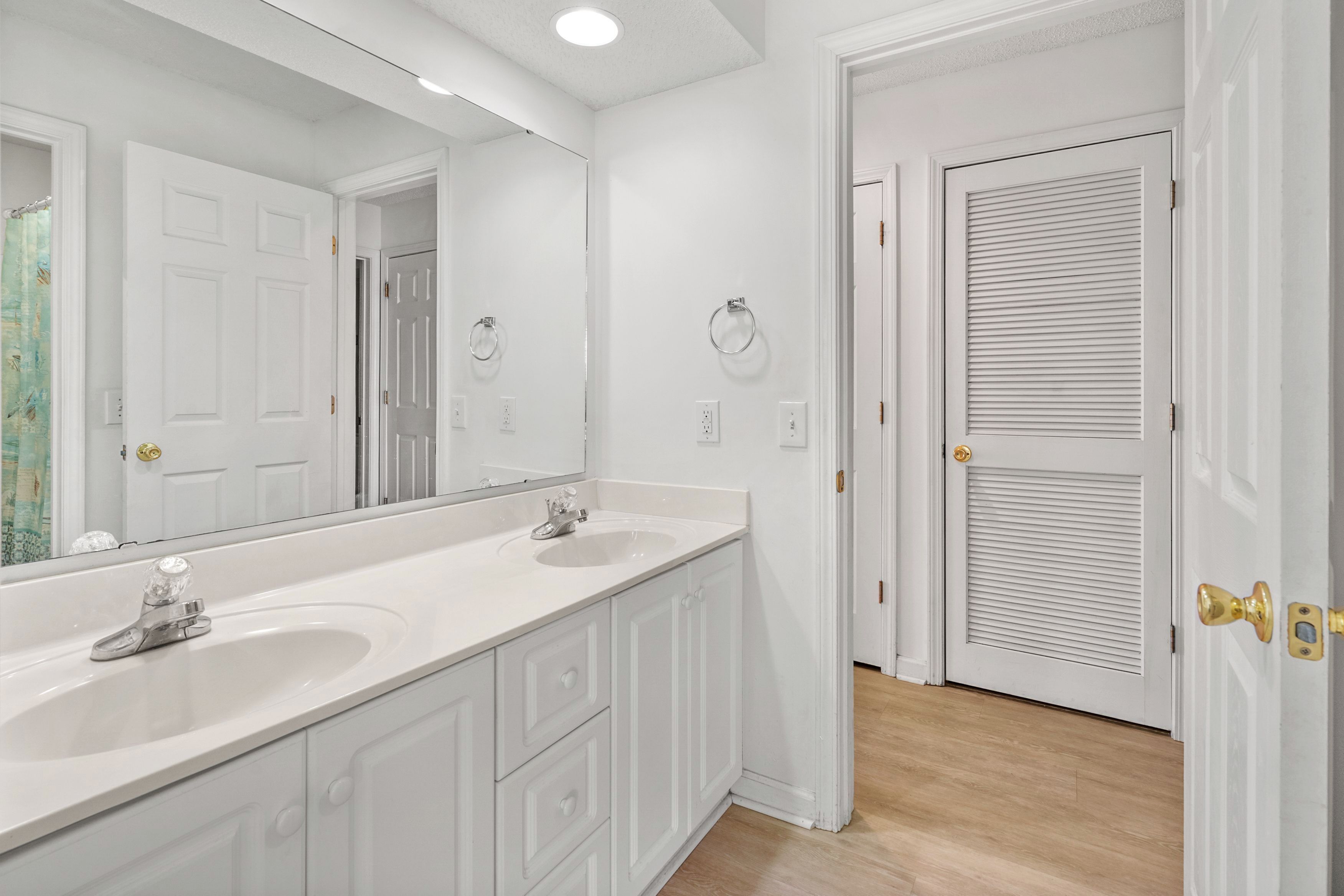 A bathroom with two sinks, a large mirror, and a walk-in closet with a sliding door.