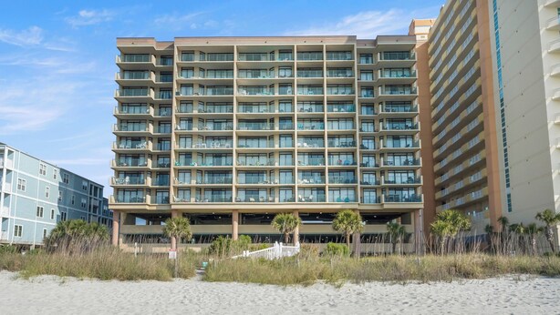 A multi-story hotel with balconies, located near a beach with sand and sparse vegetation. - Verandas 409 (North Myrtle Beach)