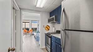 A modern kitchen with stainless steel appliances, blue cabinets, and a view to a balcony with outdoor seating. - Verandas 409 (North Myrtle Beach)