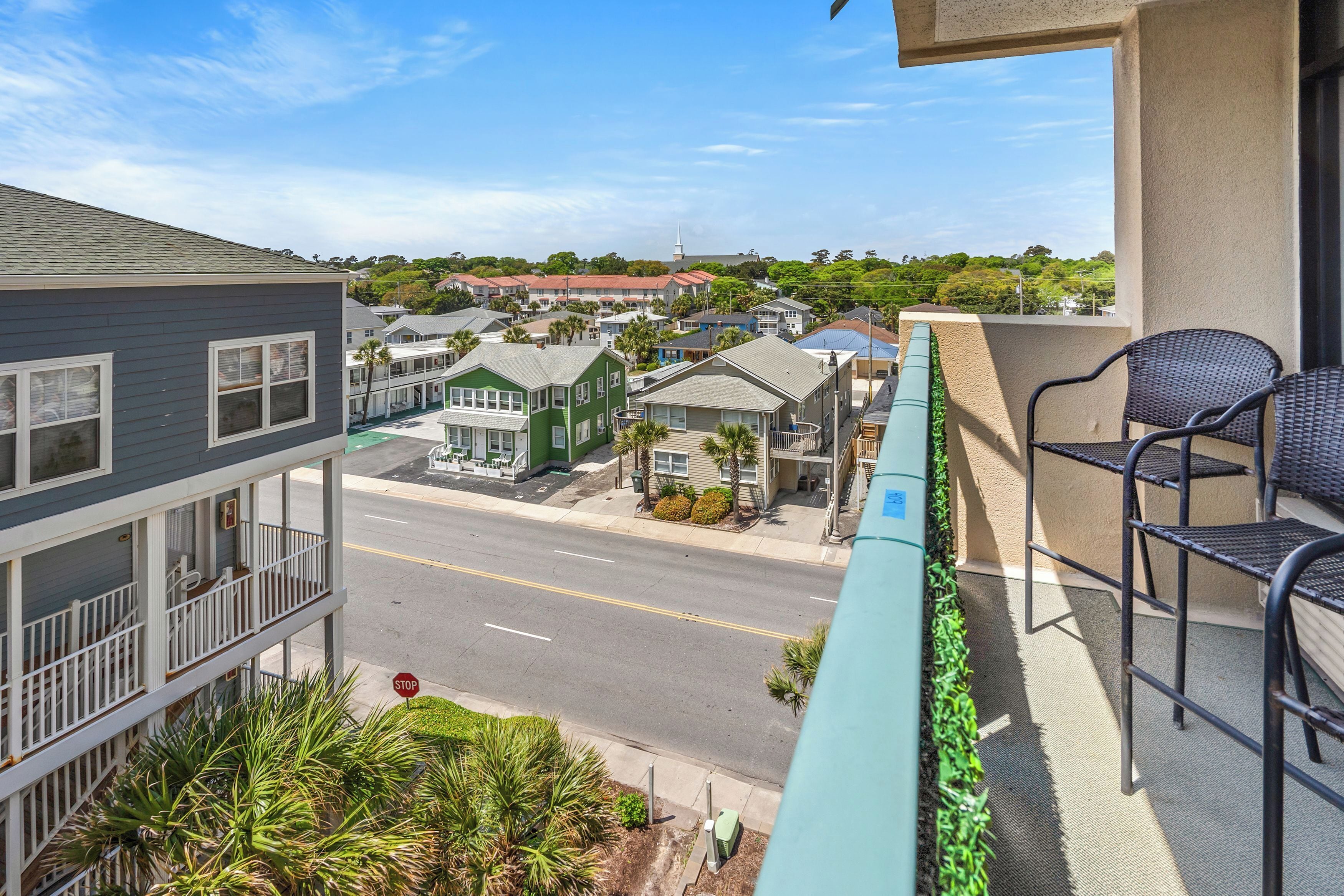 A balcony with wicker chairs, a view of a street with houses, and a stop sign.