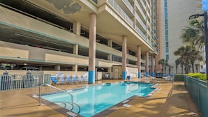 A swimming pool with a no lifeguard on duty sign, lounge chairs, and a multi-story parking garage. - Verandas 409 (North Myrtle Beach)