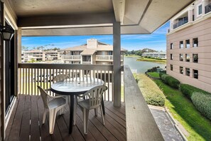 A balcony with a table and chairs, overlooking a river and a golf course. - Tilghman Lakes B3 (North Myrtle Beach)