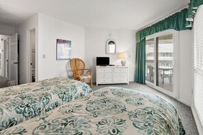 A hotel room with two beds, a television, a chair, a dresser, and a balcony with curtains. - Tilghman Lakes B3 (North Myrtle Beach)