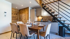 Une cuisine moderne avec un mur d’accent en bois, un coin repas avec une table dressée pour quatre personnes et un escalier doté d’une rampe en métal.