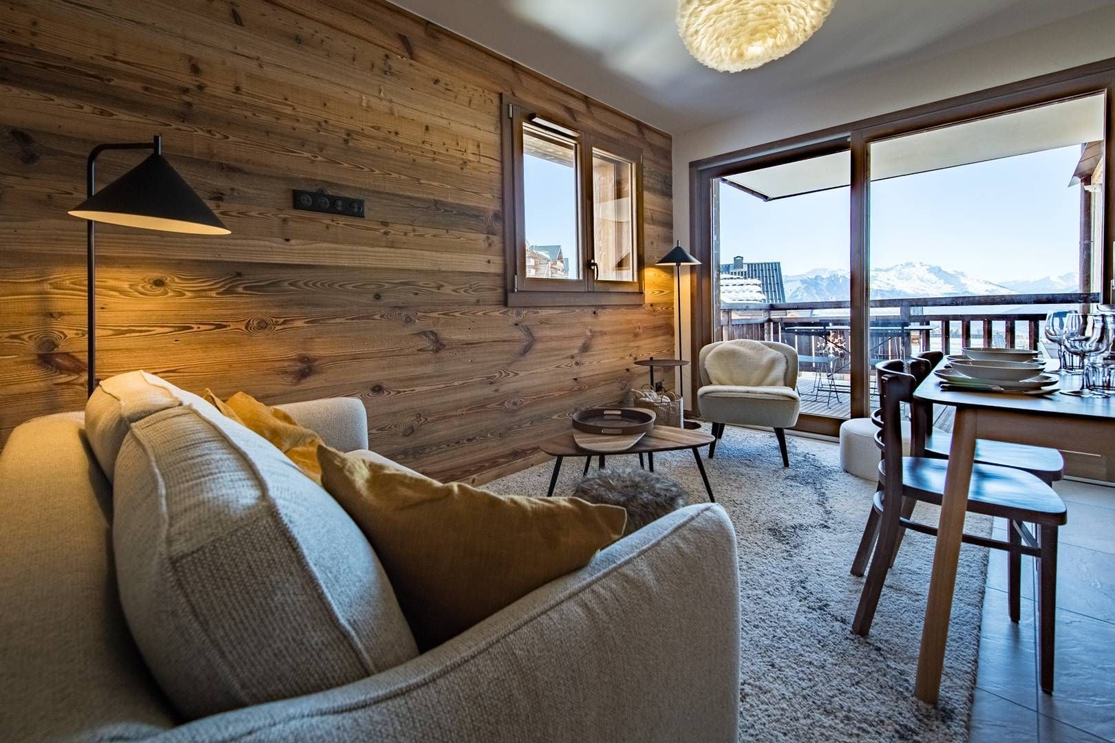 Un salon chaleureux avec un mur en bois, un canapé, une table basse et un coin repas comprenant des chaises et une table dressée.