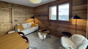 Una habitación acogedora de estilo cabaña, con decoración de madera, un sofá, una mesa de comedor y un ventanal grande.