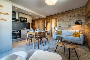 Ett modernt kök med inbyggda vitvaror, en matplats med ett träbord och stolar samt ett mysigt vardagsrum med en soffa och kuddar.