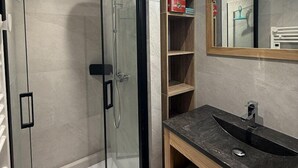 Un baño moderno con cabina de ducha de vidrio, un mueble de tocador de madera con encimera oscura y un espejo con marco de madera.