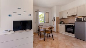 A compact kitchen with a TV, dining table, chairs, and basic appliances.