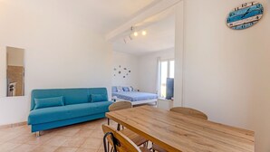 A room with a wooden dining table, a blue sofa, a bed with a blue bedspread, and a wall clock.