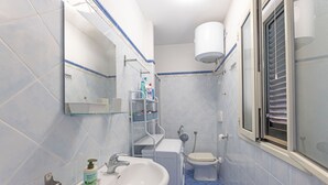 A bathroom with a sink, toilet, and a window with blinds.