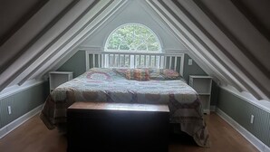 Une chambre avec une grande fenêtre, un lit recouvert d’une couvre-lit à motifs et un banc.