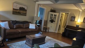 Un salon chaleureux avec un canapé en cuir marron, un fauteuil vert, une table basse en bois et un piano.