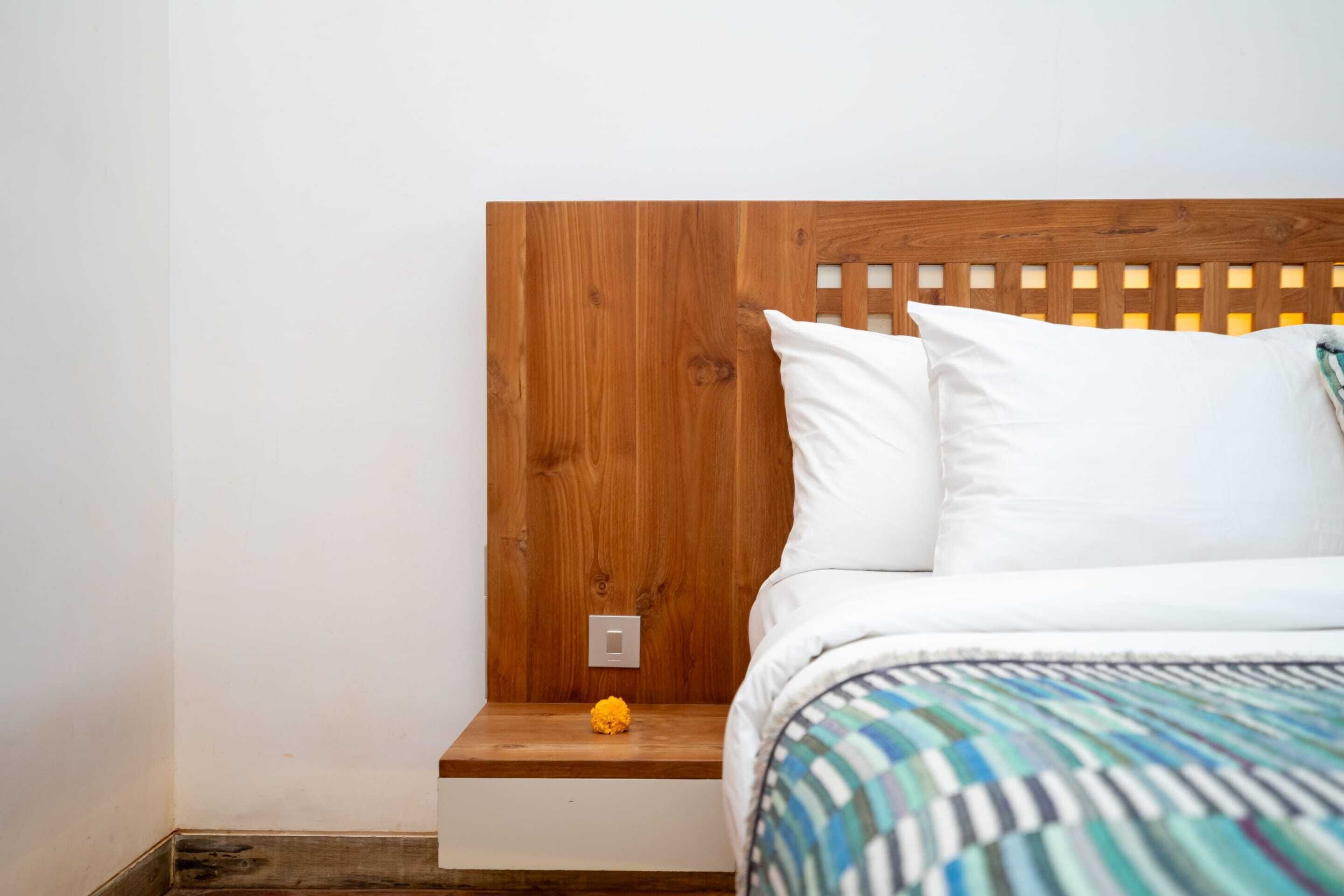 Un dormitorio con cabecera de madera, ropa de cama blanca y una mesita de noche de madera con una flor amarilla.