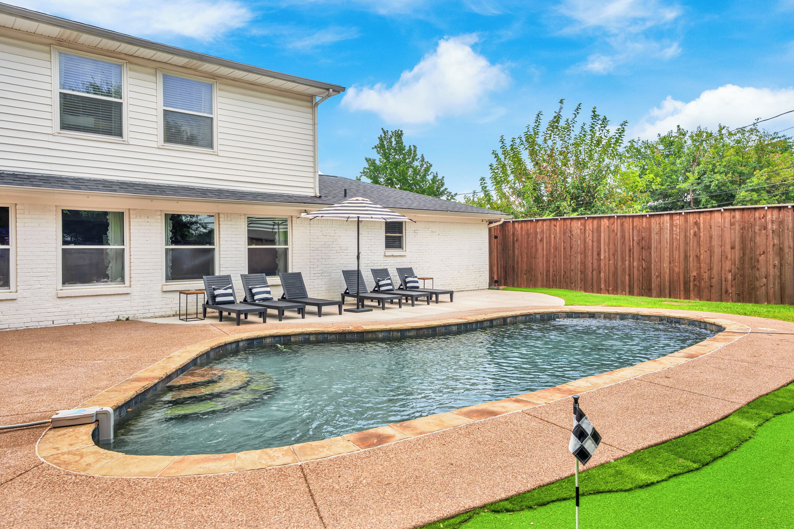 Un jardin avec une piscine, une terrasse en bois et un espace patio couvert.