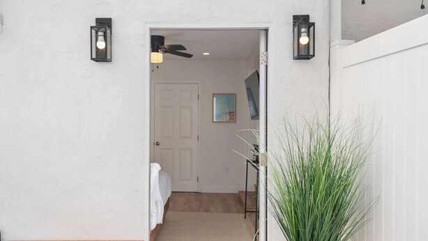 A hallway with a wooden bench, a potted plant, and a door leading to a room with a bed and a painting.
