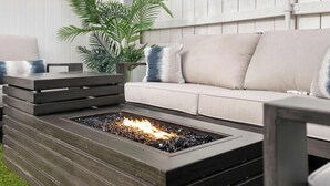 A modern outdoor seating area with a built-in fire feature, a cushioned sofa, and a wooden bench.