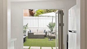 A view into a backyard with a white fence, a sofa, and a table with an umbrella.