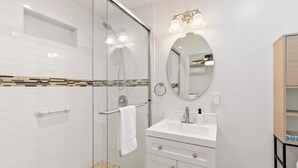 A modern bathroom with a glass-enclosed shower, a white sink with a mirror above, and a wooden cabinet.