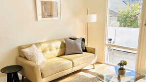 A modern living room with a beige leather sofa, a round glass coffee table, a black side table, a woven rug, a floor lamp, and a framed artwork on the wall. - Stunning Modern Self-contained Apartment (Hazelwood Park)