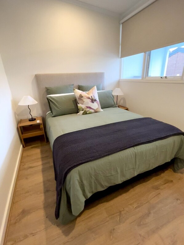 A bedroom with a bed, two bedside tables, a window, and a nightstand.