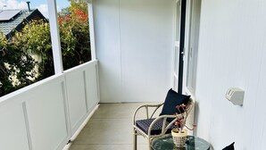 A covered balcony with two wicker chairs and a small table, a white railing, and a view of a house with a solar panel. - Stunning Modern Self-contained Apartment (Hazelwood Park)