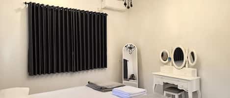 A bedroom with a bed, a vanity with mirrors, a chandelier, and a window with black curtains.
