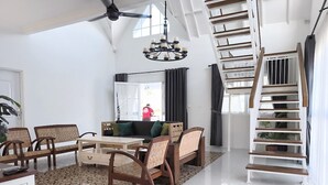 A spacious living area with a dining set, a staircase, and a view of the outdoors. - Omah Putih Menoreh (Moyudan)