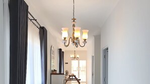 A bright, spacious hallway with a chandelier, a potted plant, and a dining area in the background. - Omah Putih Menoreh (Moyudan)
