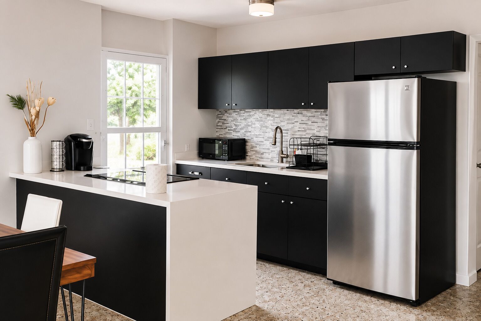 A modern kitchen with black cabinets, a stainless steel refrigerator, and a white countertop.