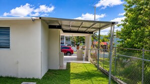 Un espacio al aire libre cubierto con un coche estacionado adentro, un jardín cercado y un edificio con una ventana y una puerta.