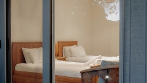 Een moderne slaapkamer met twee bedden, een houten bankje en een glazen deur naar de kamer.