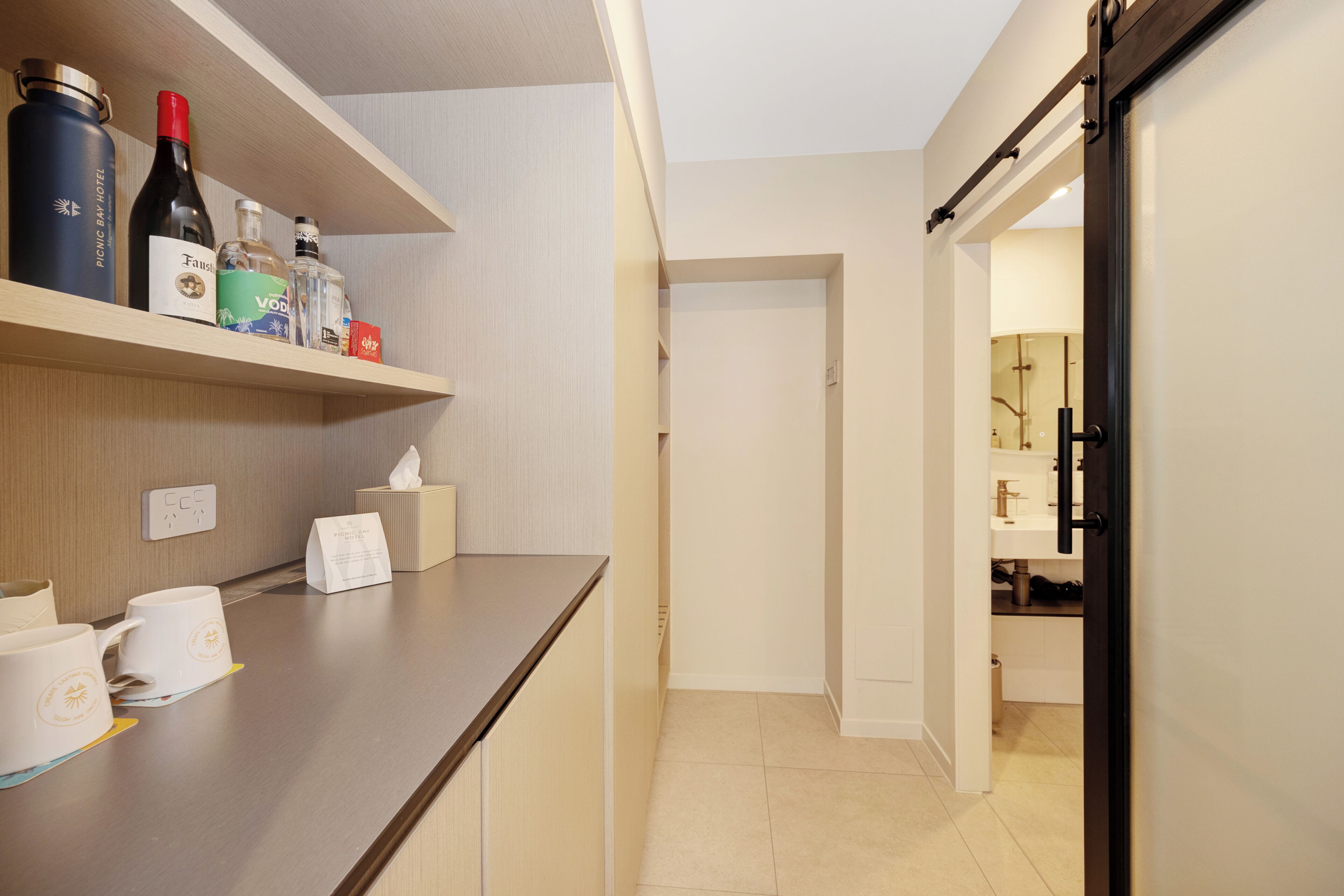 A hotel room with a wooden counter, a minibar, a sliding door to the bathroom, and a tiled floor.