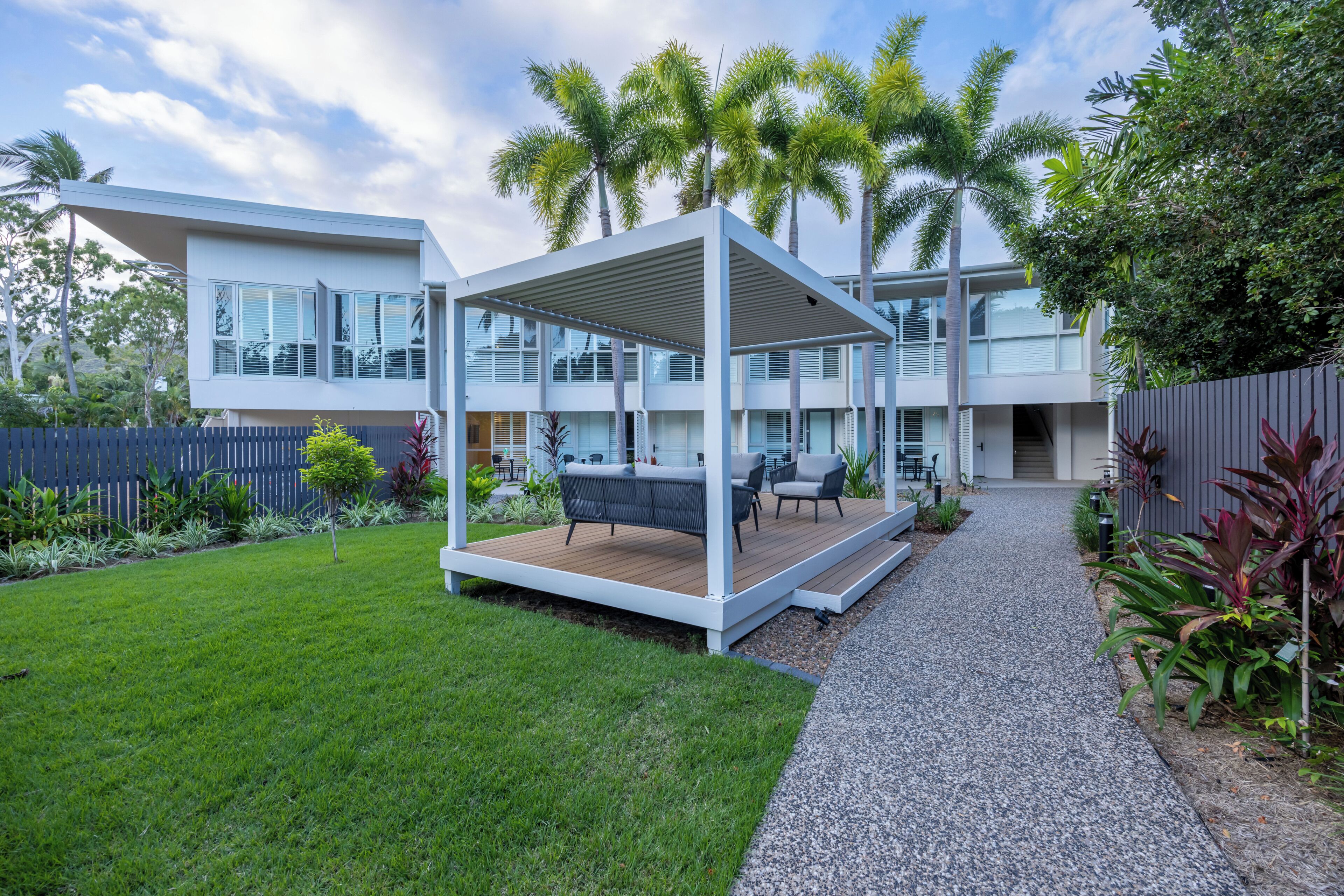 A modern house with a covered outdoor seating area, a well-maintained lawn, and a pathway leading to the entrance.