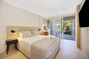 Ein modernes Hotelzimmer mit einem großen Bett, einer Nachttischlampe und Blick ins Freie durch eine Schiebetür.