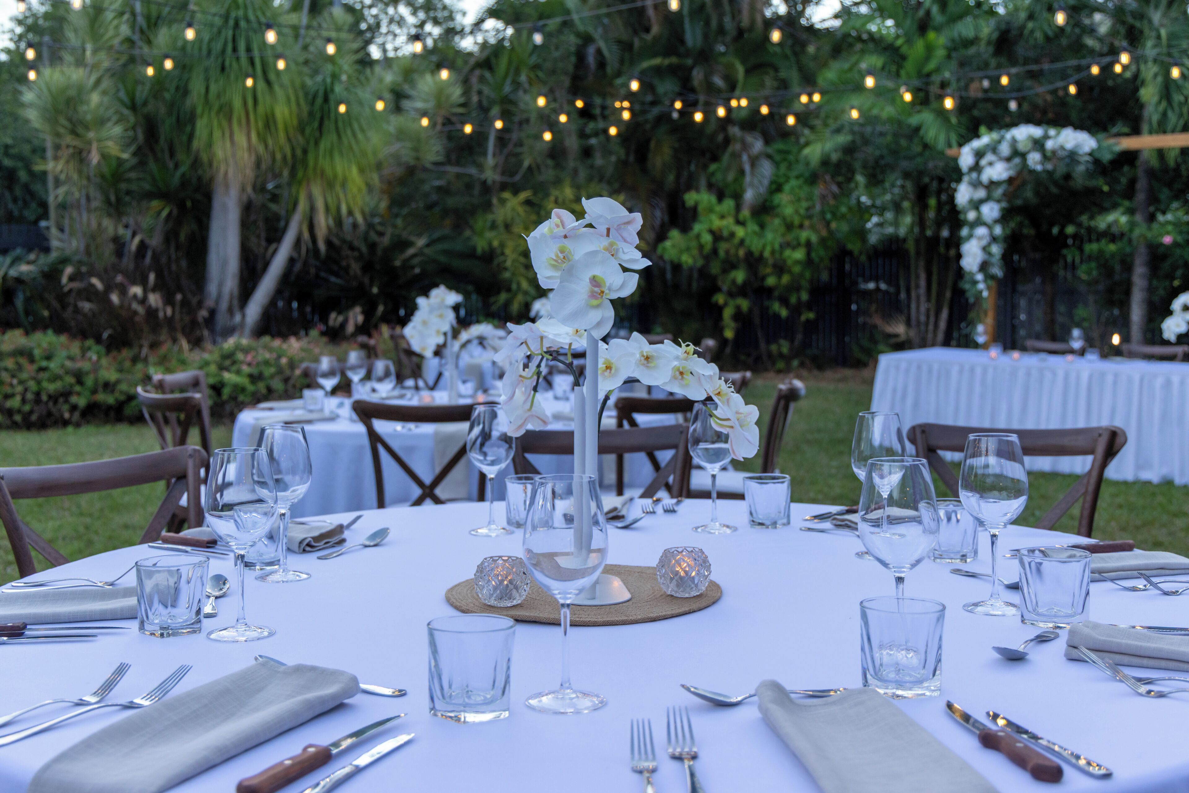 A table set for a formal outdoor event with glassware, cutlery, and a floral centerpiece.
