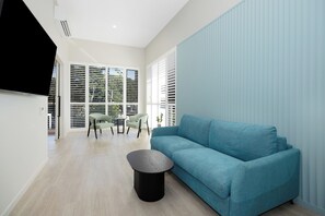 Ein modernes Wohnzimmer mit einem blauen Sofa, einem runden schwarzen Couchtisch und einem Essbereich mit Stühlen und einem Tisch.