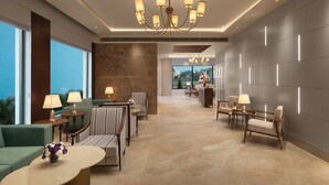 A modern hotel lobby with a chandelier, seating areas, and a view through the glass wall.
