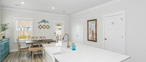 A modern kitchen with a large island, white cabinetry, and a dining area with a table and chairs.