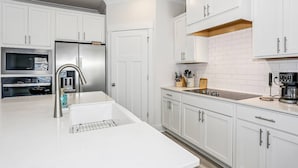 A modern kitchen with white cabinetry, stainless steel appliances, and a white countertop.