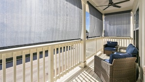 A covered balcony with wicker furniture and a ceiling fan.