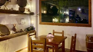 Un coin repas avec une table et des chaises en bois, une grande fenêtre donnant sur le paysage urbain nocturne, et une décoration rustique comprenant des objets en céramique exposés sur des étagères.