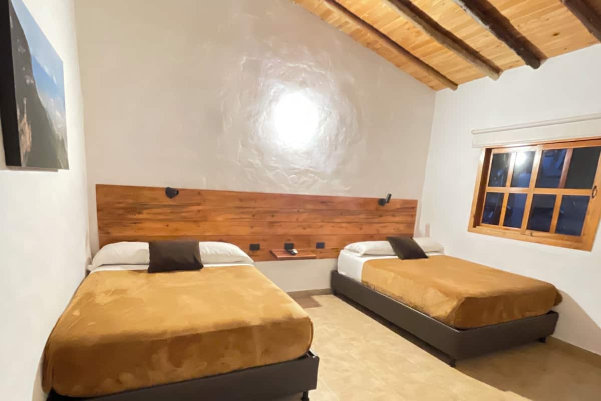 Una habitación con dos camas, vigas de madera en el techo, una ventana y una pared blanca.