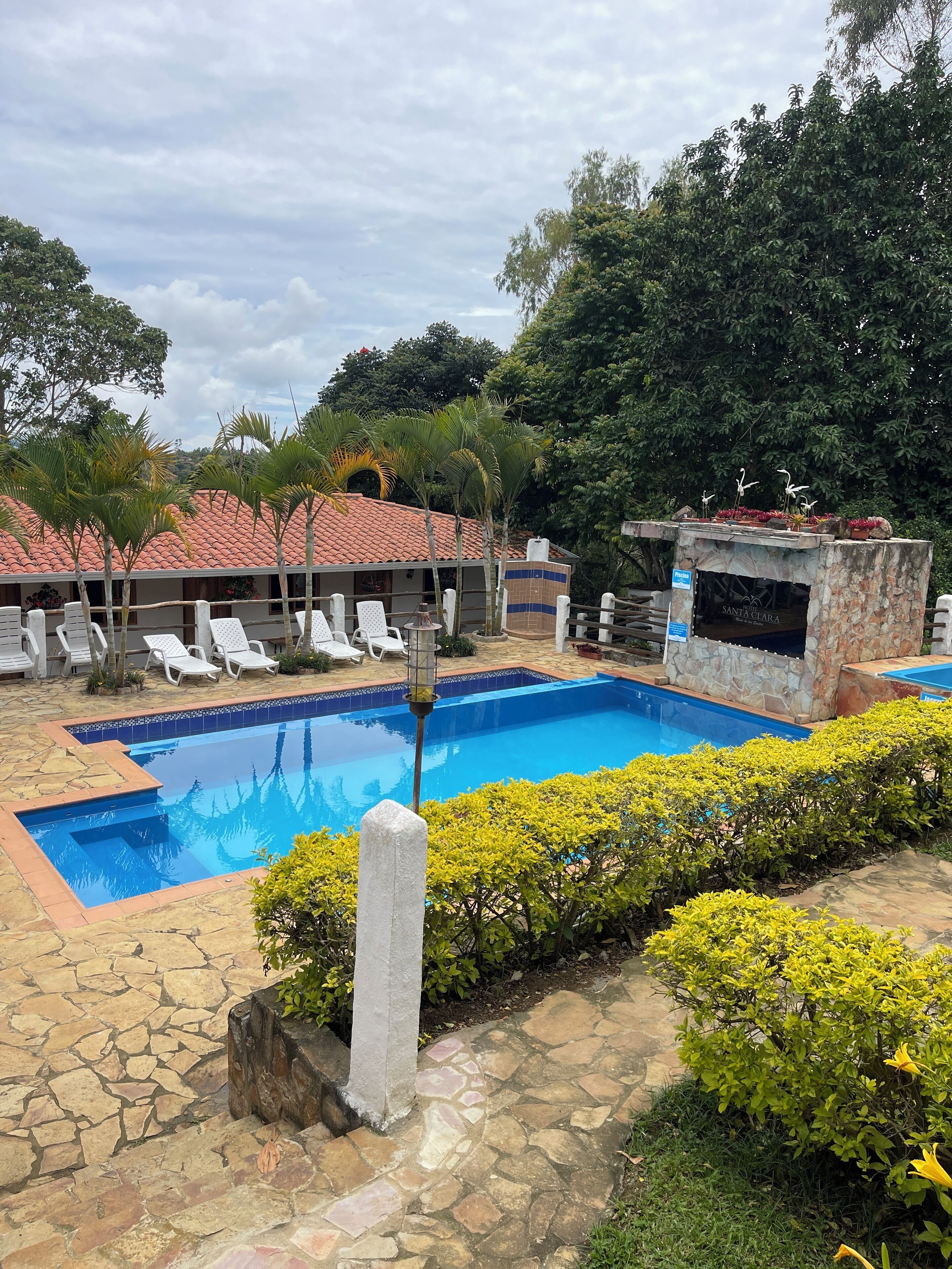 A swimming pool with lounge chairs, a stone-tiled deck, and a building with a tiled roof.