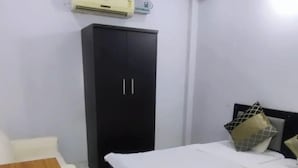 A bedroom with a bed, a wooden table, a black wardrobe, and an air conditioning unit on the wall. - Hotel Downtown  (Meerut)