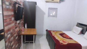 A small, clean room with a bed, a desk, and a TV mounted on a brick wall. - Hotel Downtown  (Meerut)
